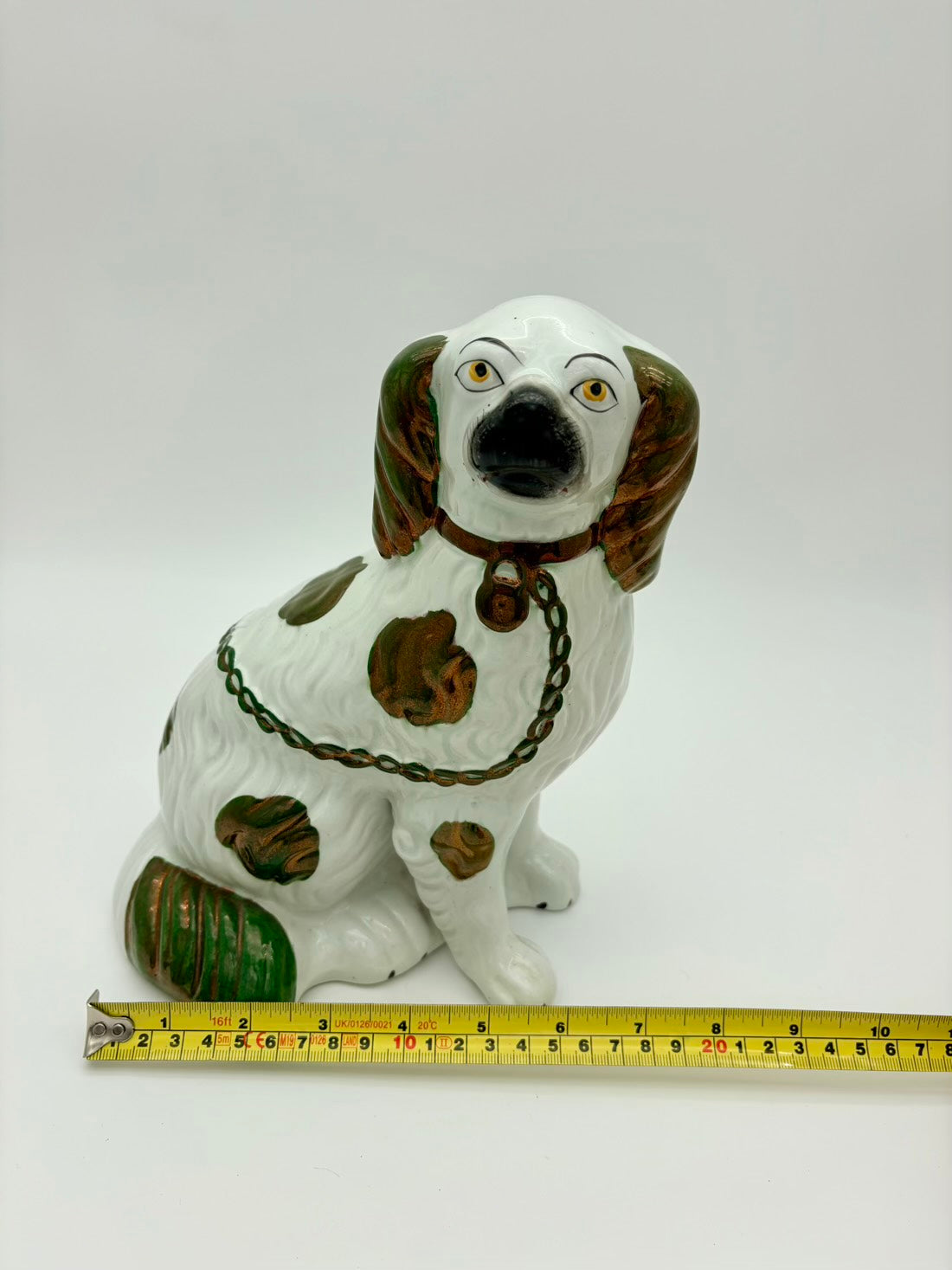 Ceramic dog figurine with a chain collar next to a measuring tape on a white background