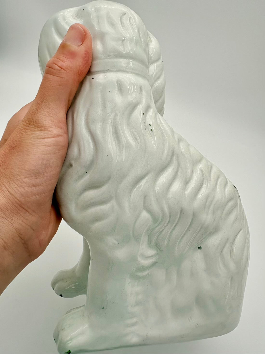 White ceramic bear figurine held by a hand against a gray background