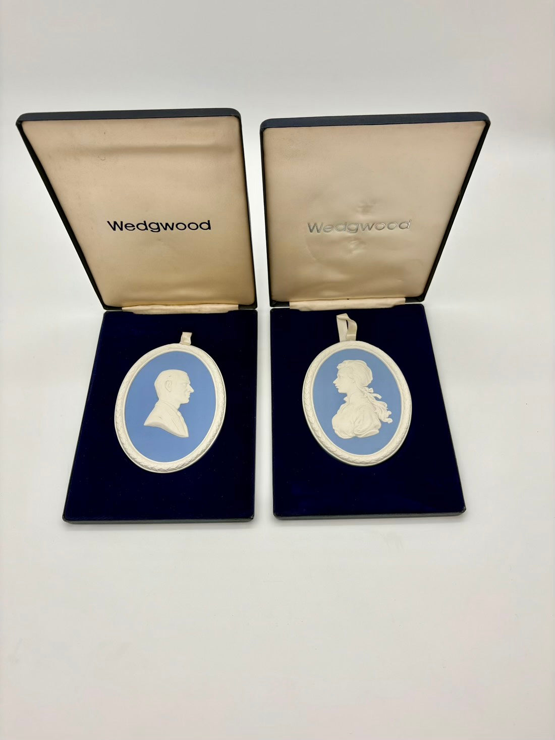 Two Wedgwood cameo brooches in open display cases on a white background
